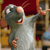 A gray cartoon rat with large ears and a white belly stands in a kitchen, holding a wooden spoon and gesturing with its right hand.
