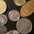Pixelated static image of multiple coins in various shades of gold, silver, and brown arranged on a dark background.