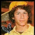 Pixelated portrait of a person with dark curly hair wearing a yellow hat and light-colored shirt against warm-toned background.