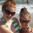 Two pixelated figures in a close-up pose, one with brown hair and dark sunglasses, the other with light brown hair, both wearing green-accented tops against a blurred background.