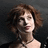 A pixelated image of a person with curly brown hair wearing a dark top and necklace, set against a dark background.