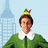 Pixelated image of a person in green elf attire with white collar and red-yellow hat, standing before city buildings under light blue sky.