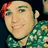 Pixelated close-up of a person with light skin, green eyes, red hair on the left side, wearing a teal patterned shirt against dark background.