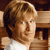 Pixelated close-up of a person with light brown hair wearing a white shirt against a wooden background.