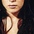 Pixelated close-up of a person's face and upper chest with dark hair, wearing a light-colored sleeveless top against a black background.