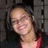 Pixelated static image of a person with light skin tone wearing dark hair and red clothing against a gray background.