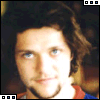 A person with curly brown hair and blue eyes wears a red-and-blue shirt, shown in three slightly different facial expressions