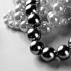 Black-and-white close-up of a beaded necklace with reflective spherical beads and a textured fabric background.