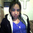 Pixelated static image of a person with dark hair wearing a blue top and dark jacket, standing against a light background with vertical elements.