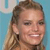 A pixelated close-up of a person with light brown hair tied back, wearing a dark earring, against a light blue background.