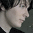 Pixelated close-up of a person's face in profile, showing light skin, dark hair, and a neutral expression against a dark background.