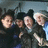 Four people in dark clothing pose closely together in a pixelated group photo with blue text listing names and a heart symbol below.