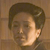 Pixelated close-up of a person's face with short dark hair, neutral expression, and light skin tone against a brown background.