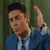 Pixelated image of a person in blue suit with white shirt and dark tie, raising right hand against green background.