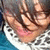 Pixelated image of a person with dark hair and light skin, wearing a white garment with black spots against a blue background.