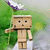 Pixelated cartoon character with blocky brown body, black eyes, and open mouth stands against green background with purple-and-white object above.