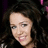 Pixelated close-up of a person with dark curly hair against a dark background with faint purple and pink accents.