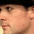 A pixelated close-up of a person's face showing eyes, nose, mouth, and ear with visible skin texture and a dark background element.
