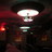 Pixelated static image showing a bright white circular light source with a greenish base against a dark background with red and brown tones.