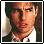 Pixelated static image of a person's face with light skin tone, brown hair, and dark eyes wearing a white shirt against a blurred background.