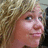 Pixelated close-up of a person with light brown curly hair and fair skin, showing partial facial features against a blurred background.