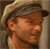 Pixelated static image of a man's face wearing a cap, with visible dithering and low-resolution rendering artifacts.