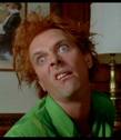 Static image of a person with red hair wearing a green shirt, set against an indoor background with framed pictures and furniture.