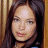 A pixelated image of a person with long dark hair against a wooden background, next to green text reading 'OriginalIcons.com' on a solid green backdrop.