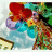 Pixelated static image with red, blue, green, yellow, purple, and brown hues forming abstract shapes against a light background.
