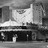 Static grayscale image of a building facade with a prominent sign displaying 'CINEMA' in block letters, set against a pixelated background.