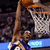 Pixelated image of a basketball player in mid-air shooting a ball toward a hoop with net, wearing purple and gold uniform against dark background.