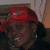 A person wearing a red cap with a white logo, dark clothing, and earrings, smiling broadly in a of four
