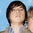 Pixelated image of a person with dark hair against light blue background, wearing plaid shirt and holding hand near head.