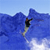 Pixelated static image of a person skiing down a snowy slope with blue mountains in the background under a light blue sky.