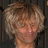 Pixelated close-up of a person with light brown curly hair against dark vertical lines.