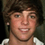 Pixelated close-up of a person with dark brown hair, light skin tone, and visible teeth in a neutral expression wearing a white shirt.