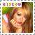 Pixelated image of a person with long brown hair wearing pink clothing, holding hand near face against green background; text "HILARY" above with heart symbol.