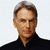 Pixelated portrait of a person with short graying hair wearing a dark high-collared shirt against a light background.