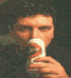 A person in a dark shirt holds a white cylindrical object with orange and black markings, then drinks from it, and finally holds it again.