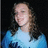 Pixelated image of a person with long brown hair wearing a light blue top against dark background.