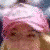 A person with light brown hair wears a pink headscarf and white clothing, positioned against a blurred background.