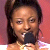 Pixelated close-up of a person with dark hair holding a black microphone against a pink background.
