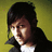 Pixelated portrait of a person with dark hair wearing a black jacket over white shirt against yellow-green background.