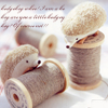 A soft-focus image of a small hedgehog-like creature resting on a spool of brown thread, with additional spools and blurred text in the background.
