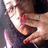 Pixelated close-up of a person with light skin and dark hair, wearing a dark top with pink accents, holding a red object near their face.