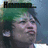 Pixelated image of a person with green hair wearing a dark hat, mouth open in a shout, against a blue background with partial text above.
