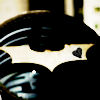 A static icon featuring a black bat symbol with white accents on a dark background, partially obscured by motion blur effects.