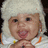 Pixelated image of a smiling child with light skin, dark eyes, and light hair wearing a white head covering and white clothing with orange and yellow accents.