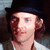 Pixelated close-up of a person wearing a dark hat and light-colored shirt, with visible ear and hair details.