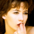 Static pixelated close-up of a person's face with light brown hair and hand near mouth, rendered in warm tones on dark background.